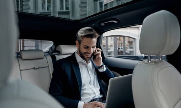Handsome young man in full suit talking on smart phone and smiling while sitting in the car